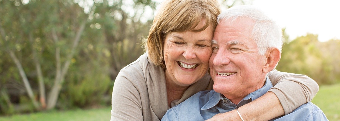 Older couple smiling together after denture tooth replacement consultation