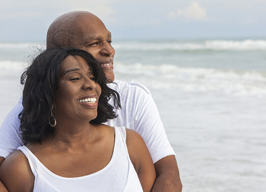 An older couple hugging at the beach.